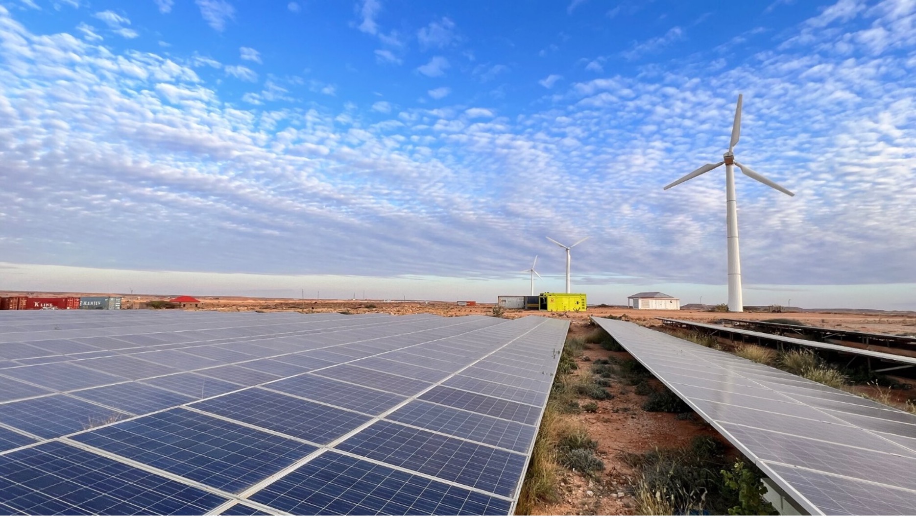 solar panels in the foreground and wind power in the background on a mostly blue sky
